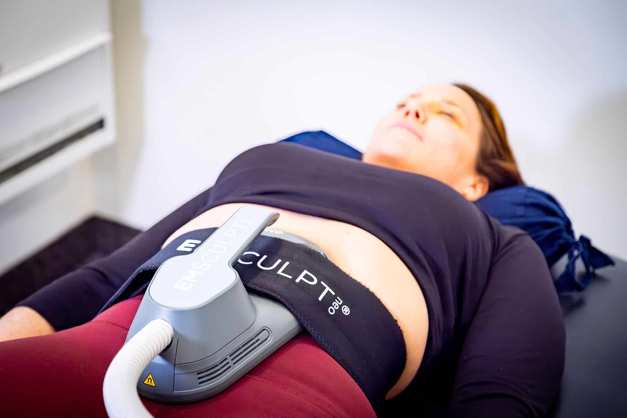 Patient relaxing during an Emsculpt Neo body contouring treatment, with the applicator secured to the abdominal area in a clinical setting.