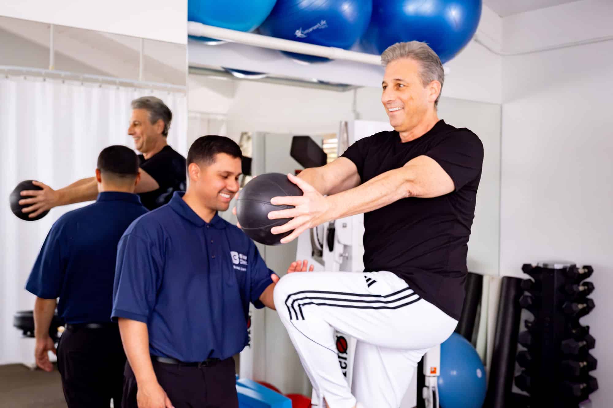 Physical therapist guiding a patient through a balance and core-strengthening exercise with a medicine ball in a rehabilitation clinic.
