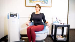 Woman seated on an Emsella chair for a non-invasive pelvic floor treatment at Bissell Clinic in Santa Barbara.