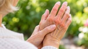 Senior woman massaging painful, inflamed arthritic knuckles, a candidate for laser therapy in Santa Barbara
