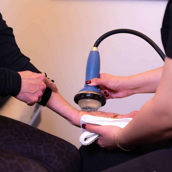 Therapist using shockwave therapy device on patient’s forearm for pain relief treatment