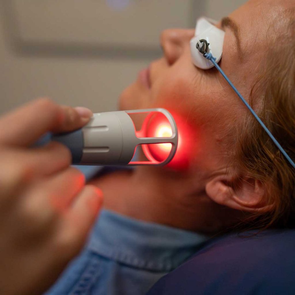 Practitioner applying Emvital laser therapy to a patient's jaw and neck for TMJ pain relief at Bissell Clinic